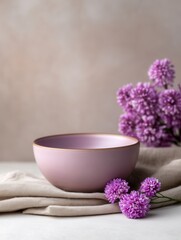 Pink Ceramic Bowl Rests Serenely on a Linen Cloth, Adorned With Vibrant Purple Flowers in a Quiet Studio Setting