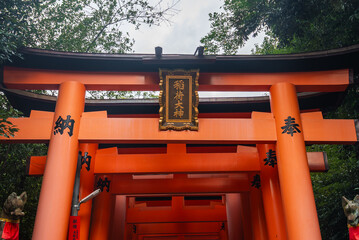 Vermilion torii gates rise in sequence at Fushimi Inari Taisha in Kyoto, Japan, a gilded plaque...