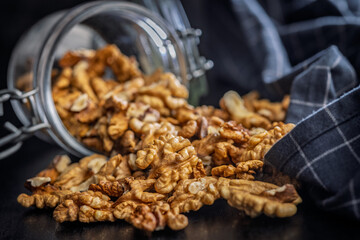 Peeled walnut kernels in jar on black table.