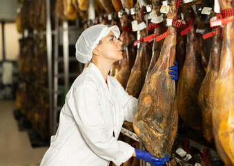 Factory worker checks the hanging ham. Technologist controls the quality of the ripening of the jamon.