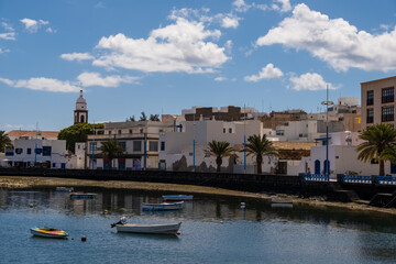 Arrecife Lanzarote showcasing colorful boats in the harbor set against a backdrop of historic buildings and volcanic mountains. The lively scene captures the island's vibrant coastal life