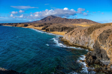 Aerial Panoramic view of Playa Papagayo's golden sands and turquoise waters surrounded by rocky cliffs. Visitors enjoy sunbathing and swimming under clear blue skies. Scenic and tranquil atmosphere