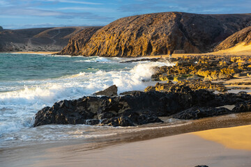 Panoramic view of Playa Papagayo's golden sands and turquoise waters surrounded by volcanic rocky cliffs on sunset