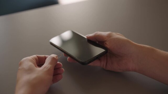 Close-up cropped shot of man using sim ejector tool into smartphone to remove or replace subscriber identity module, signifying mobile phone maintenance, upgrade, data transfer, slow motion.
