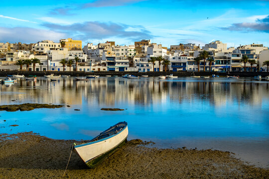 Vibrant scene of Arrecife Lagoon in Lanzarote featuring numerous boats floating peacefully in clear waters. Modern buildings and distant mountains complete the tranquil backdrop - Powered by Adobe