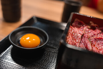 A close view shows marinated beef in a red box and a raw egg yolk on a tray in a Japanese restaurant in Nara, Japan, with warm light and shallow focus.