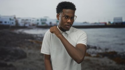 Man pointing finger on rocky sandy beach by rolling blue sea; confidence resolve challenge motivation.