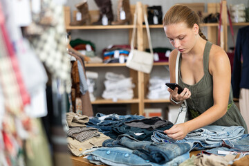 Woman holds phone in hands and scans barcode labels on jeans to pay for purchases through app. Modern payment methods by qr. Woman takes pictures of jeans and sends photo to stylist