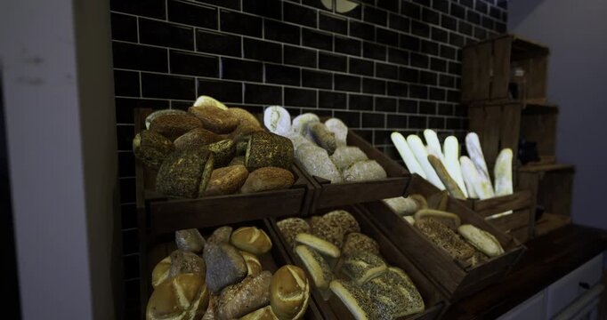 Various types of artisan breads are arranged on wooden shelves in a charming bakery. The warm ambiance invites customers to explore the selection of freshly baked goods.