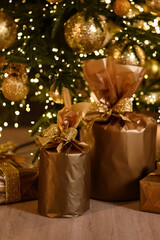 Close-up of elegant golden Christmas gifts wrapped with shiny ribbons under a decorated Christmas tree, surrounded by sparkling lights and festive ornaments.