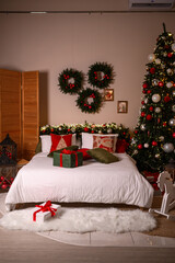 Cozy festive bedroom decorated for Christmas with a beautifully lit tree, holiday wreaths on the wall, seasonal pillows, and wrapped gifts placed on the bed and floor, creating a warm and joyful