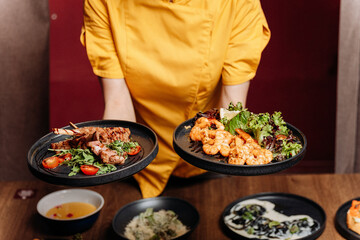 Chef presenting shrimp salad and grilled ribs on black plates in a modern restaurant