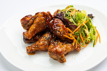Glazed chicken wings with sesame and fresh slaw on white plate, studio top view