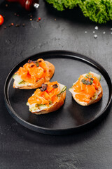 Top view of salmon canapes on baguette with cucumber and cream cheese on black plate