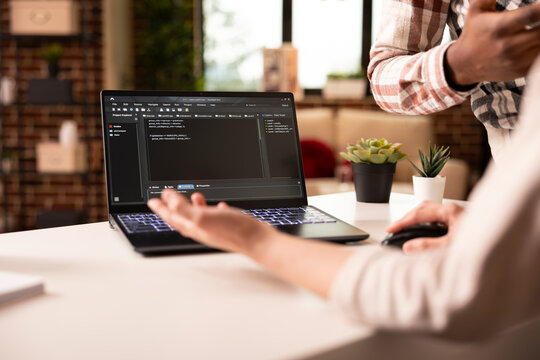 Closeup on laptop displaying programming language as multiethnic people discuss on building an app from home. Diverse couple brainstorming and debugging code for web development in modern apartment.