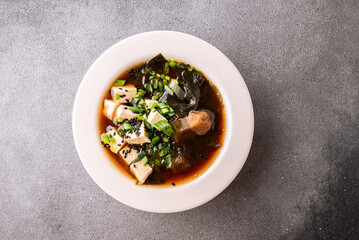 Fresh traditional miso soup with tofu, shiitake mushrooms, green onion, sea mustard and spices on grey stone background with copy space for your design. Traditional Japanese cuisine. 