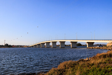 Long modern bridge spanning wide lagoon waters under clear blue sky, Portugal, Q.ta das Ricos, 9...