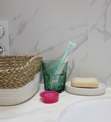 A clean and minimalist bathroom scene: the composition includes a toothbrush holder with toothbrushes, a bar of soap, woven basket