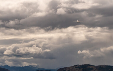 Commercial airplane ascending into dense, overcast clouds after taking off from Jackson Hole Airport in Jackson, Wyoming. The sky is filled with dramatic, dark gray clouds, creating a moody atmosphere