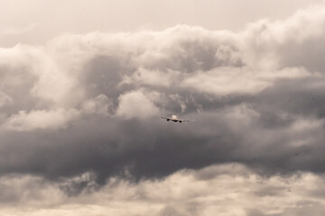 Commercial airplane climbing into dense, overcast clouds The sky is filled with dramatic, dark gray clouds, creating a moody atmosphere