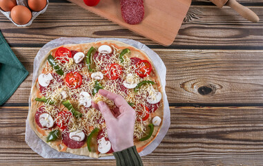 Step 14: Woman's hands sprinkle grated cheese onto pizza dough on a wooden table.