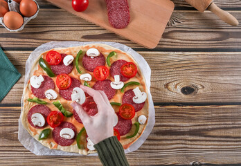 Step 13: Woman's hands arrange sliced mushrooms for pizza dough on a wooden table.