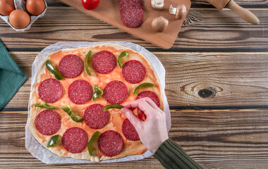 Step 11: Woman's hands place peppers for pizza dough on wooden table.