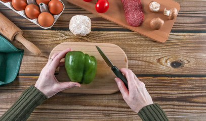 Step 9: A woman's hands prepare to cut peppers for pizza dough on a wooden table.