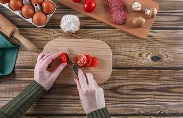 Step 11: Woman's hands cutting tomato for pizza dough on a wooden table.