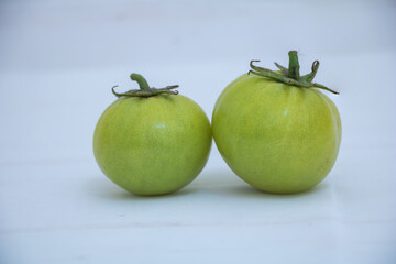Two green unripe tomatoes on white background