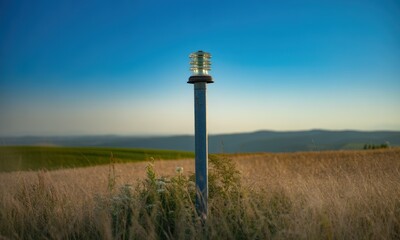 A metal utility pole with a glass insulator, in a golden field