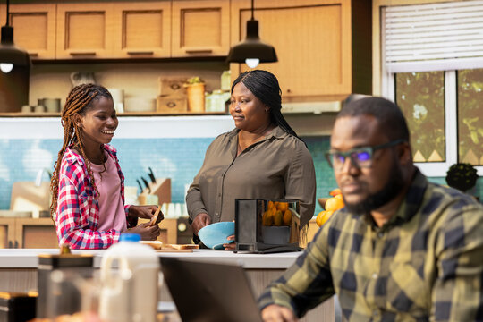 Black woman and her daughter preparing breakfast for dad and brother, discussing with family and bonding during morning routine. Mother getting the kids ready with meal prep. - Powered by Adobe