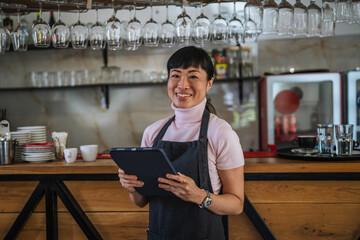 Asian woman owner holding tablet in bar