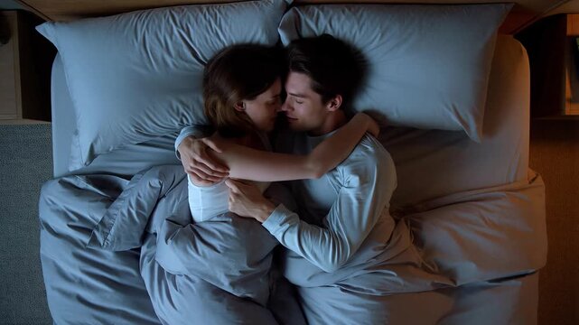young adult couple lying close together and embracing affectionately in bed under the covers at night, enjoying a quiet, intimate, and romantic moment of rest and togetherness