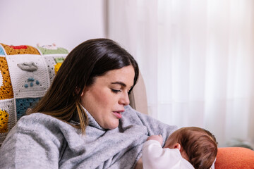 Naklejka premium Mother breastfeeding newborn baby at home in cozy setting
