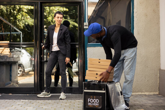Pizza delivery courier handing a pile of boxes to a woman waiting outside. Cheerful efficient food takeaway service showcasing professionalism and positive meal delivery interaction.