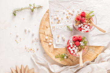 An overhead shot of two glasses of layered raspberry and chia seed pudding with fresh raspberries and white crowberry on a rustic wooden platter