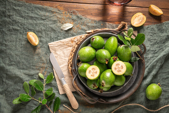 Overhead shot of a rustic still life with ripe pineapple guavas, some cut open to reveal the fleshy pulp, on a small plate and in a basket