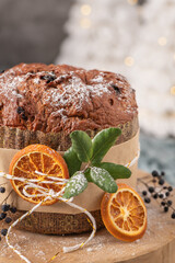 Vertical detailed shot of a sugar-dusted panettone, wrapped and tied with twine, garnished with dried orange and frosted holly leaves