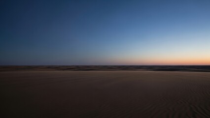 A vast desert landscape at dusk with a gradient sky from blue to orange.