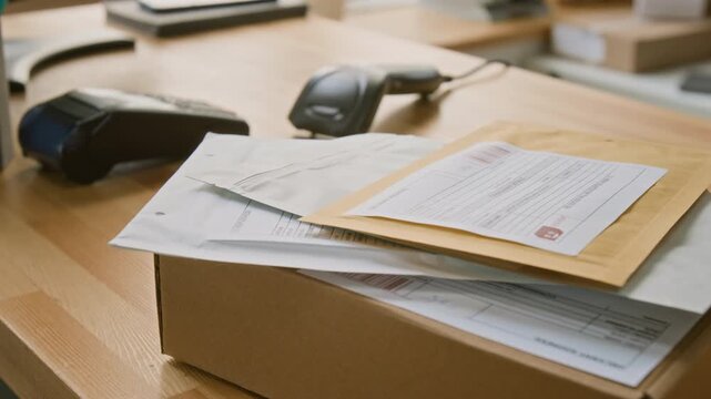 No people close-up of package with consignment invoice, letters or business documents in envelopes, barcode scanner and card payment terminal, on customer service desk at express delivery company