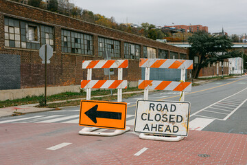 Road closure signs direct traffic on a quiet urban street beside brick buildings in fall