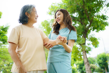 Obraz premium Caregiver assisting elderly Asian woman during a walk in the garden.