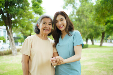 Caregiver assisting elderly Asian woman during a walk in the garden.