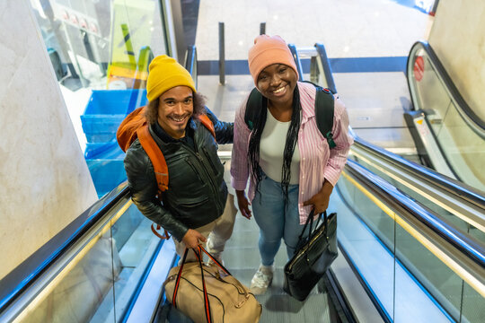 Young couple traveling on escalator with luggage, smiling