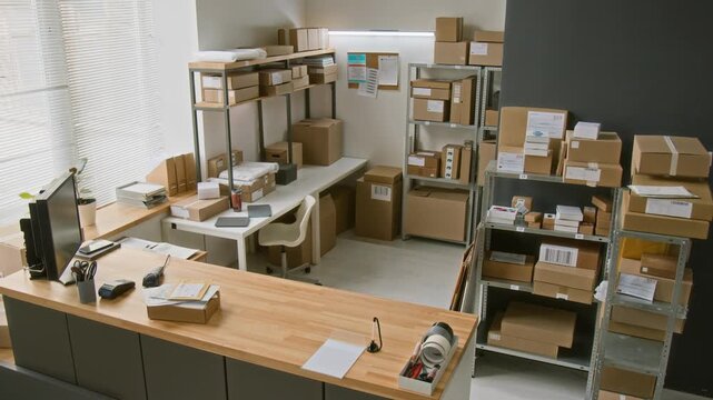 High-angle surveillance camera shot of express courier delivery company office, with customer service counter, racks of assorted parcels and packages on racks, ready for shipment, at workday