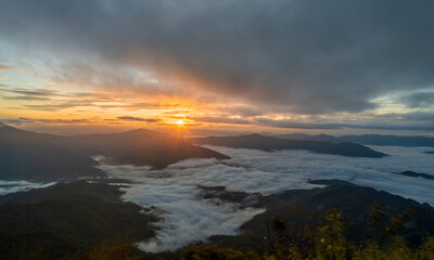 Sunrise shining through clouds over mountain and misty valley, beautiful natural morning scene.