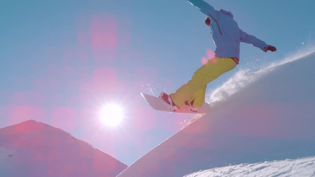 SLOW MOTION, LENS FLARE: Snowboarder leans into a powerful slash turn high above a sunlit peak, kicking a sparkling plume of powder as he crashes. Playful backcountry freeriding in the European Alps.