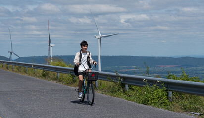 Asian teen boy rides bicycle near wind farm on sunny countryside road.