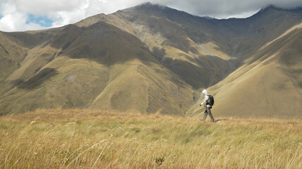 A traveler hiking alone on golden mountains under soft sunlight, exploring nature and freedom.